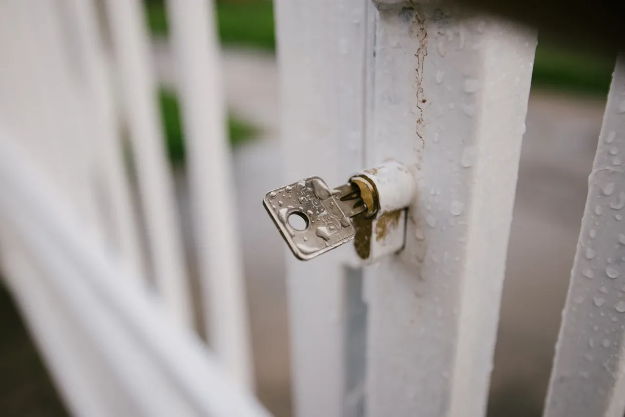 Key inserted in a white metal gate lock with visible water droplets, photographed in May 2020