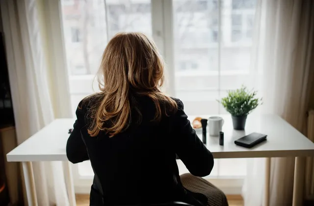 Woman seated at a desk beside a window, illustrative home-work photograph