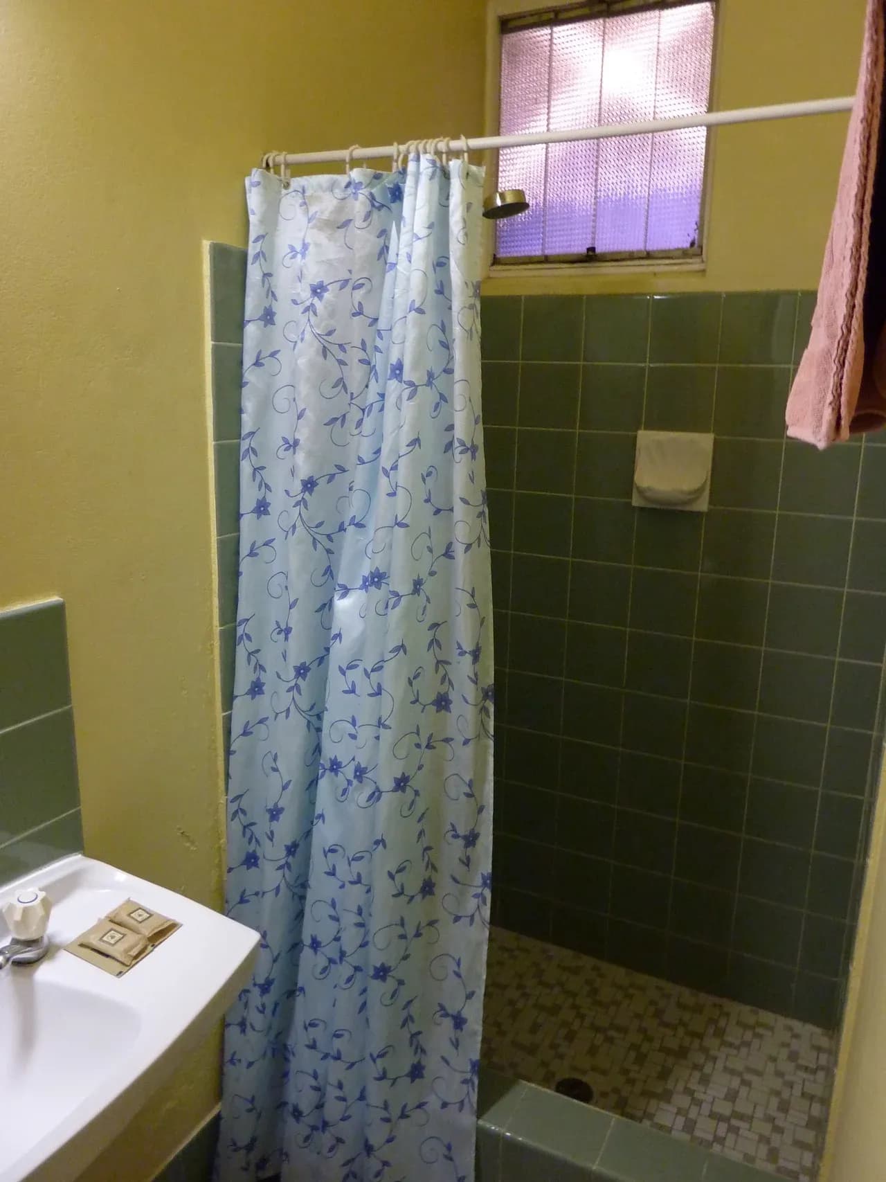 Bathroom with green tiles, patterned shower curtain, frosted window and part of a basin at accommodation in Yass, New South Wales, Australia