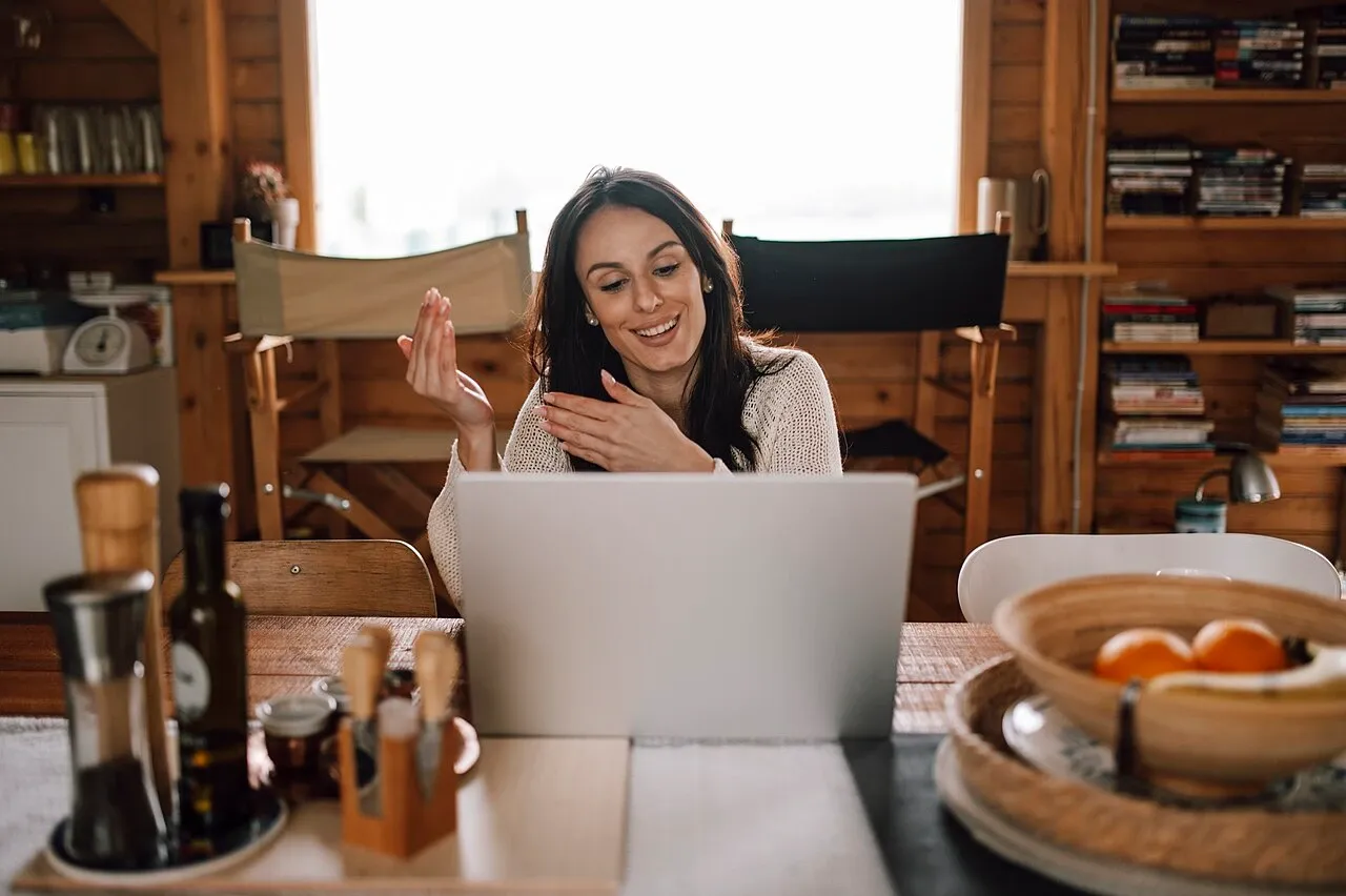 Woman gesturing while seated behind a laptop at a wooden table, photographed in May 2026