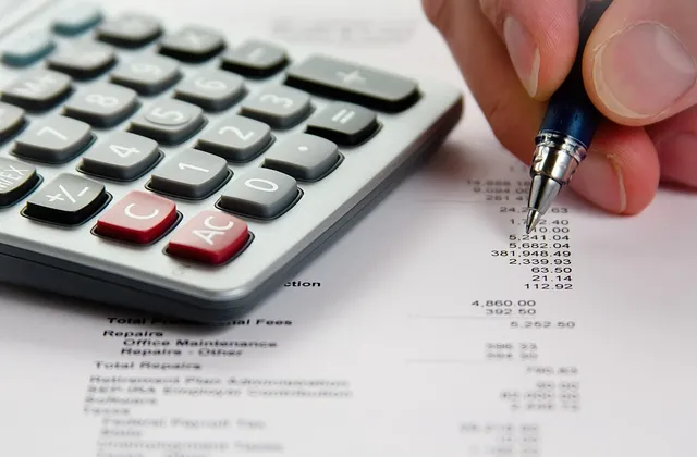 Hand holding a pen beside a calculator and printed financial figures, illustrative photograph from October 2010