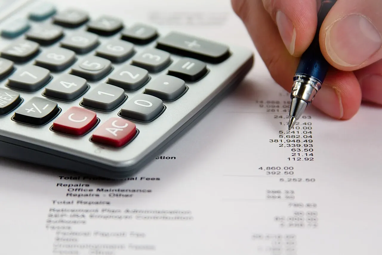 Hand holding a pen beside a calculator and printed financial figures, illustrative photograph from October 2010