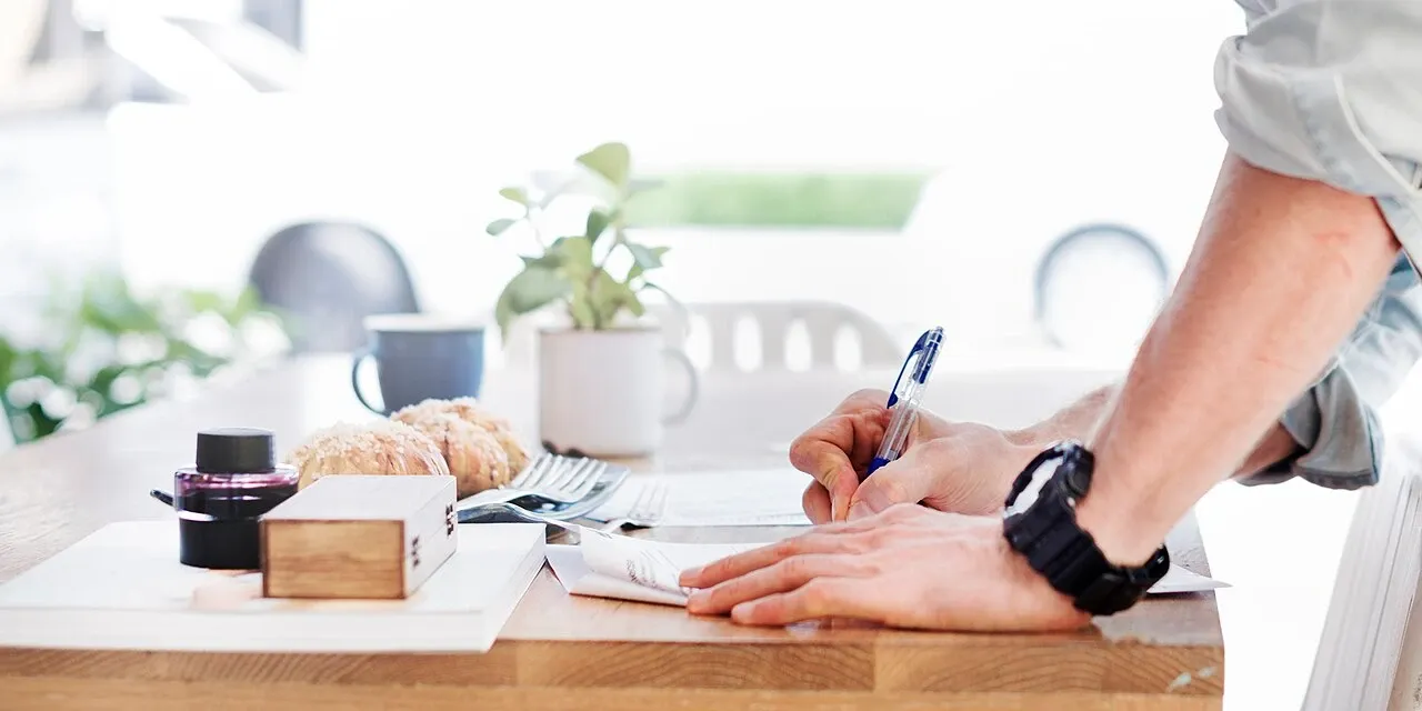Man writing on papers at a wooden table in Bangkok, Thailand, illustrative stock photograph