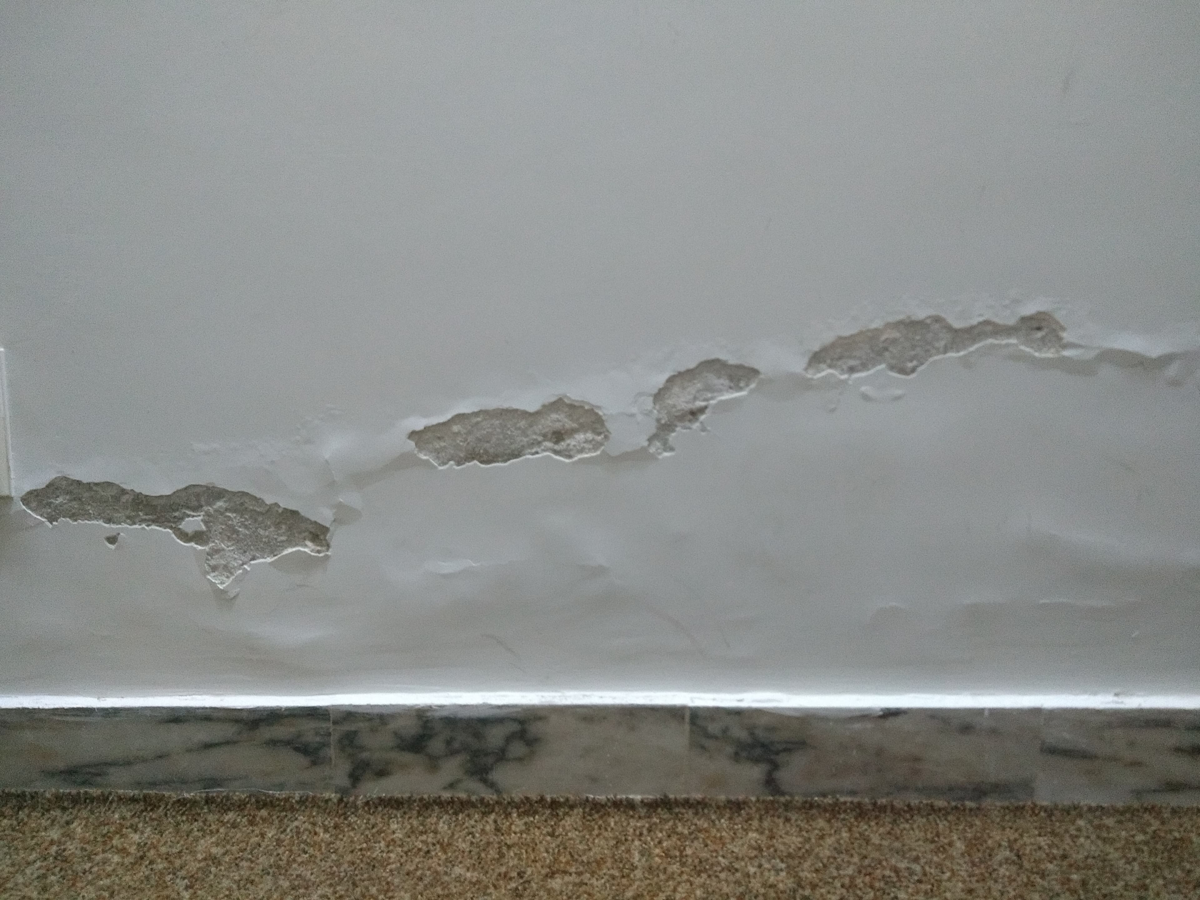 Damaged plaster and moisture marks along the lower part of an interior wall