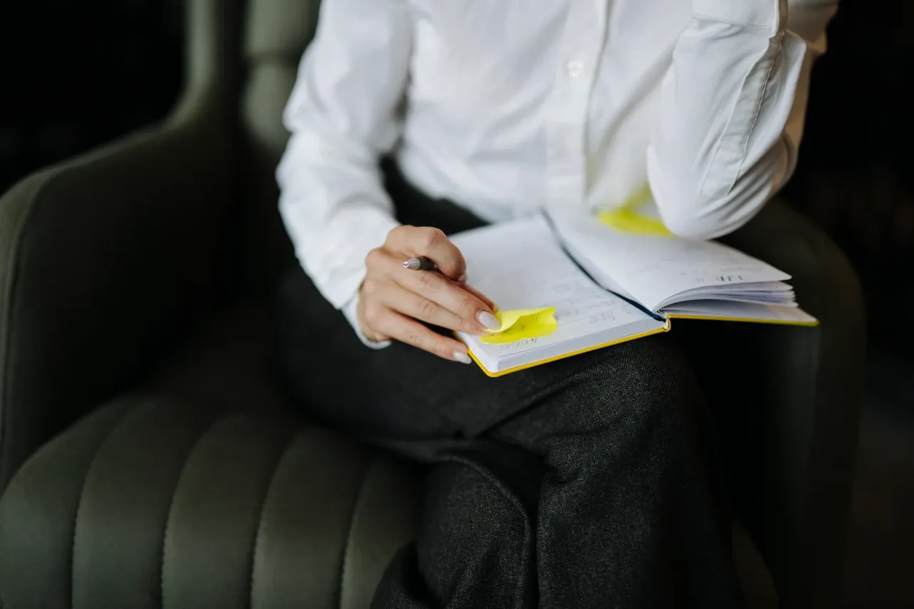 Person writing in an open notebook with sticky notes while seated in an armchair, photographed in June 2026