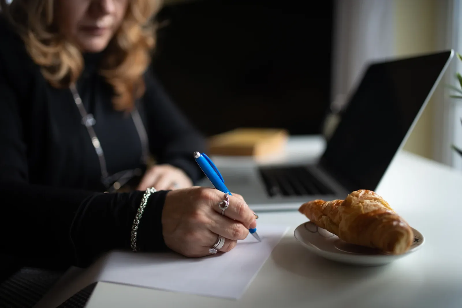 Hand writing notes beside a laptop on a desk, illustrative photograph