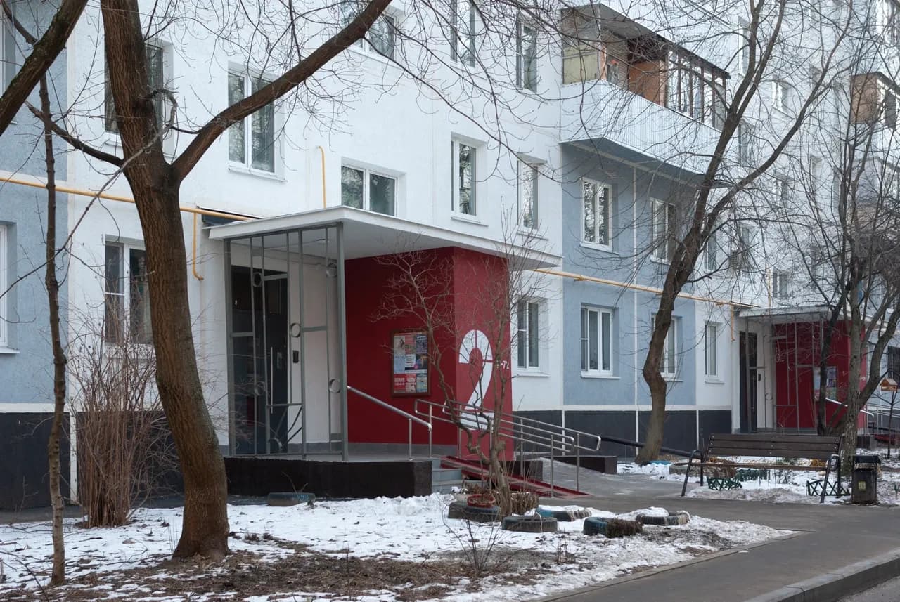 Covered apartment entrance with steps, a ramp and railings beside snow-covered ground in Moscow, photographed in March 2025
