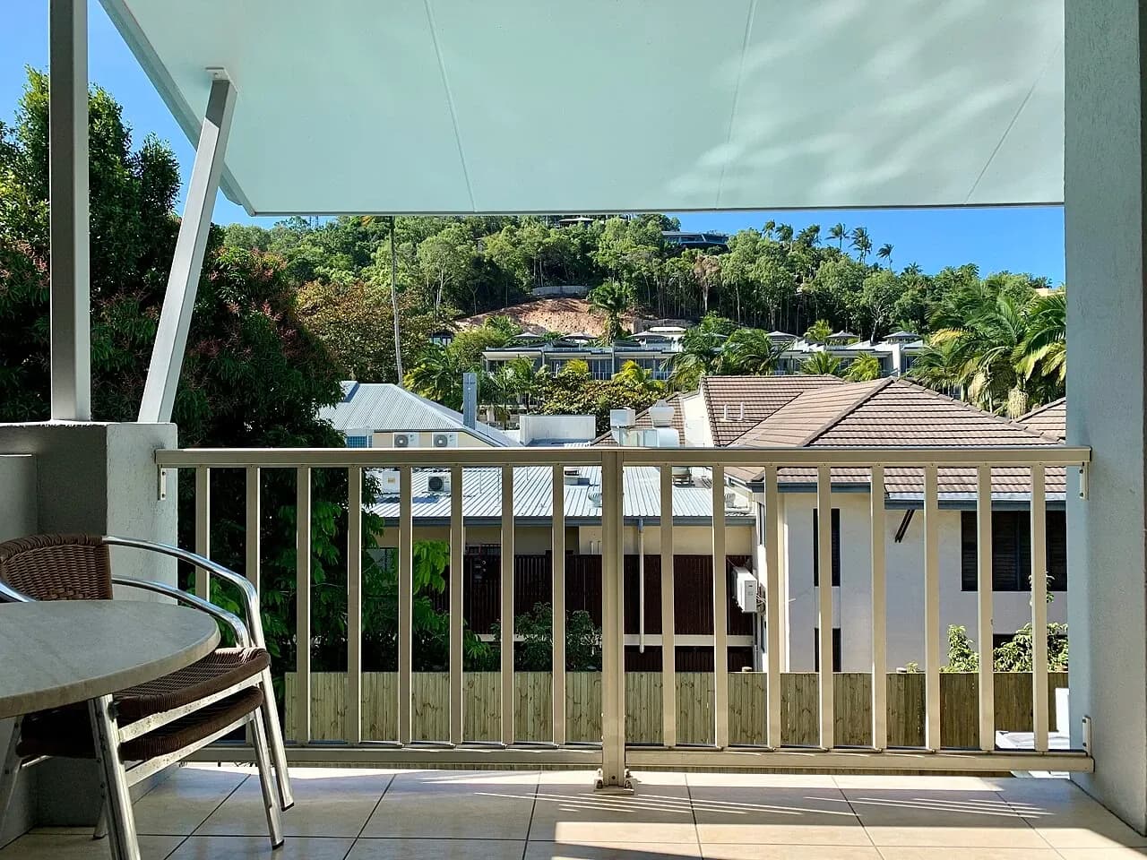 Covered balcony with a table overlooking nearby buildings and vegetation at accommodation in Port Douglas, Australia