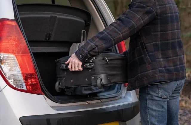 Person placing a black suitcase in a car boot, illustrative February 2022 photograph