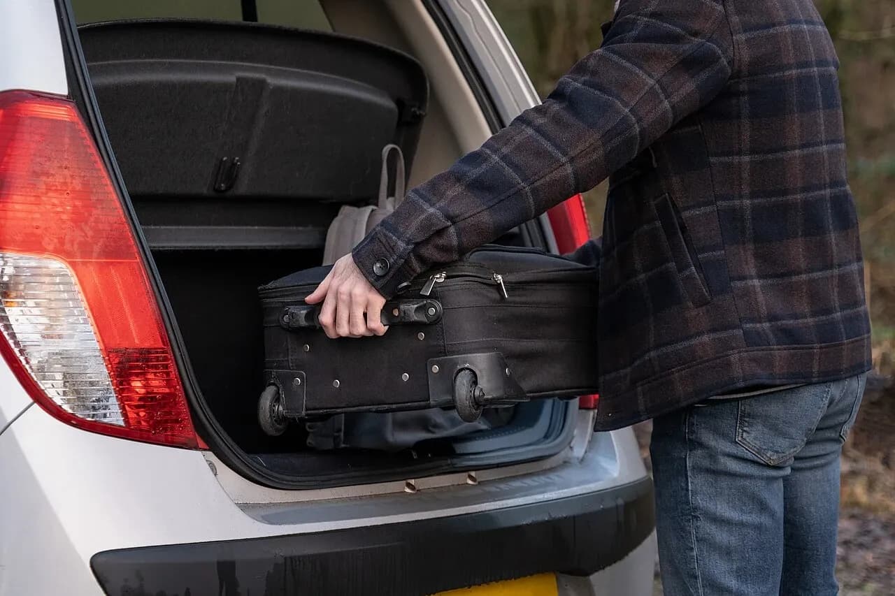 Person placing a black suitcase in a car boot, illustrative February 2022 photograph