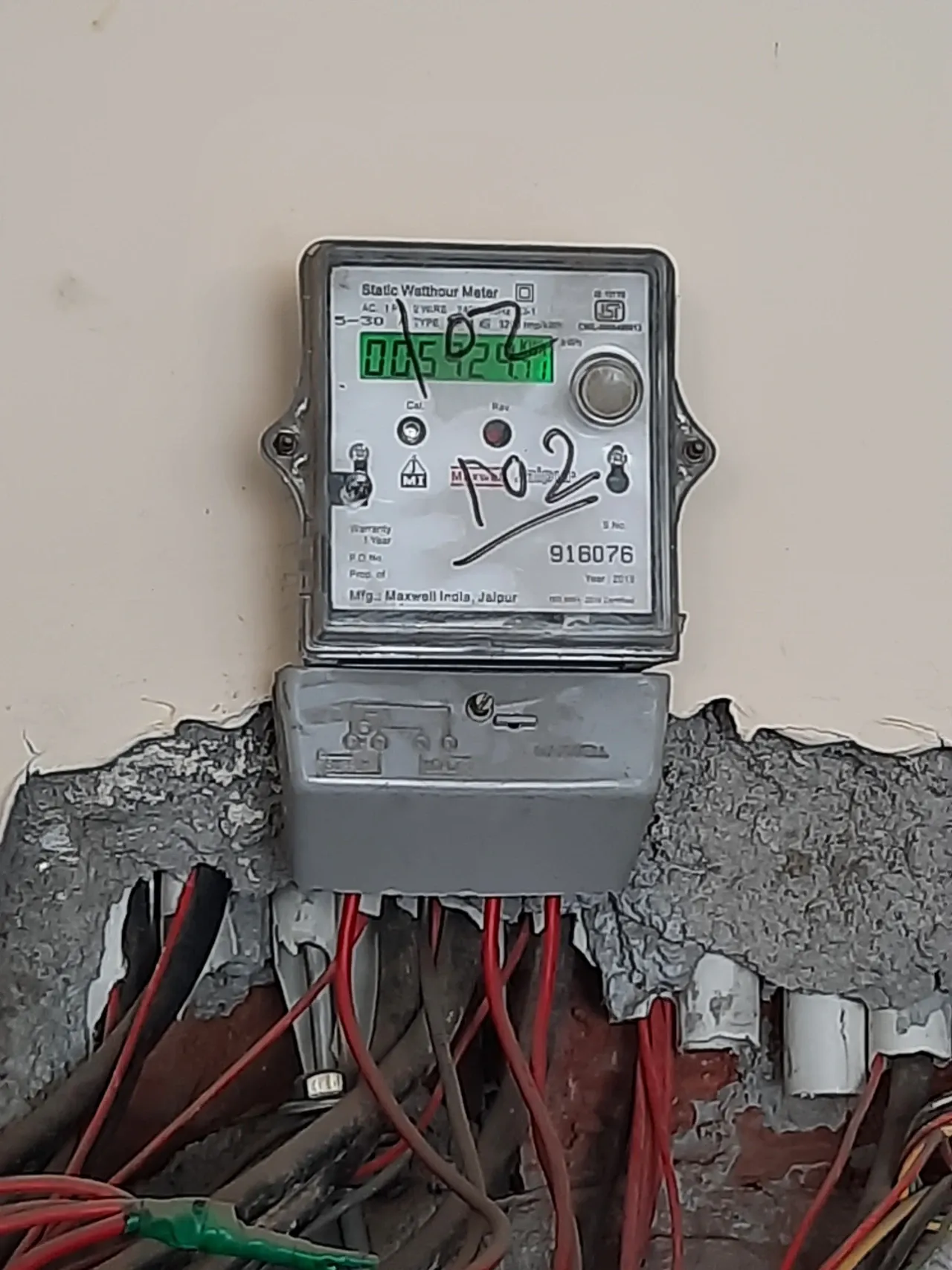 Wall-mounted electricity meter with a green display and cables below in an Indian household, photographed in July 2022