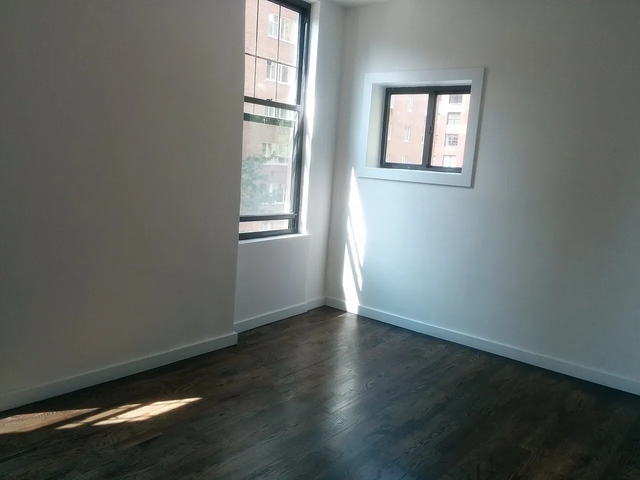 Sunlight falling across wooden flooring beside two windows in an unfurnished apartment room, photographed in August 2018