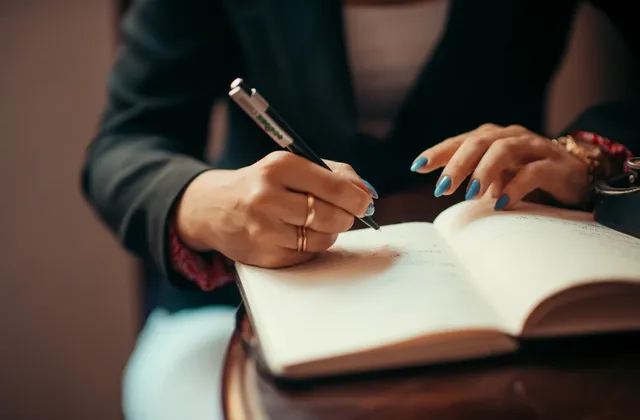 Hands holding a pen and writing in an open notebook on a desk