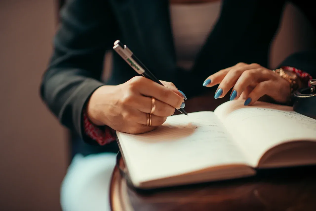 Hands holding a pen and writing in an open notebook on a desk