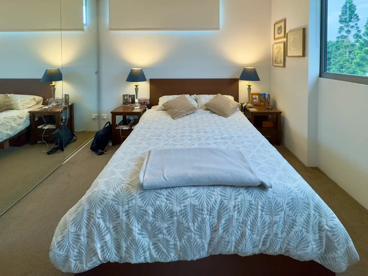 Brisbane apartment bedroom with a made bed, bedside lamps, a mirrored wardrobe and a window, June 2025
