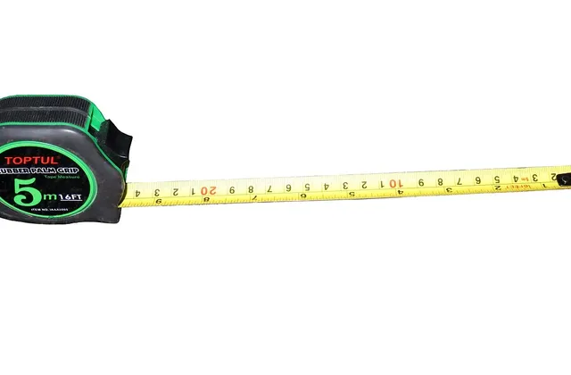 Green and black retractable tape measure with its yellow tape extended on a white background