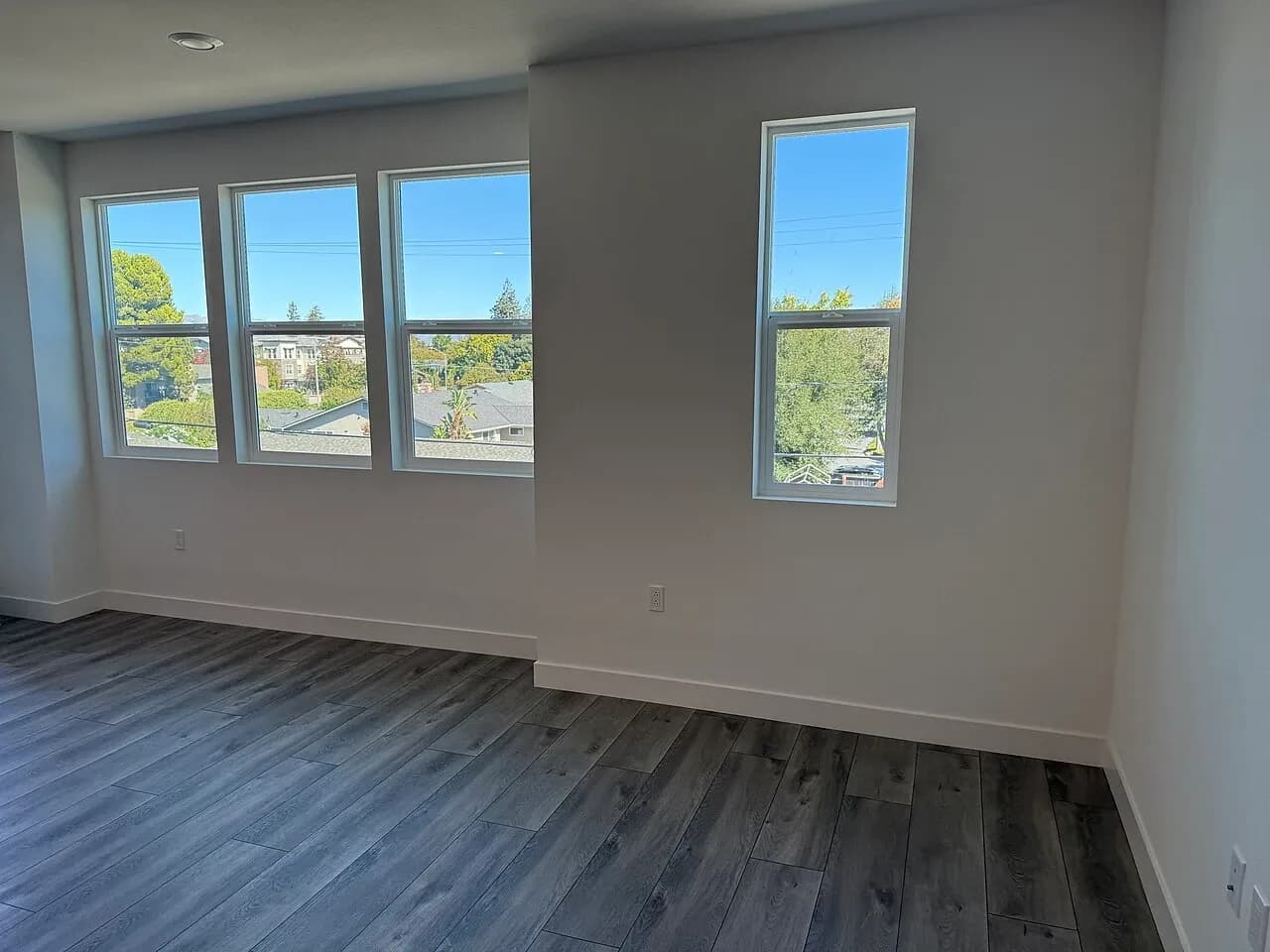 Unfurnished apartment room with a row of windows overlooking nearby roofs and trees in the United States