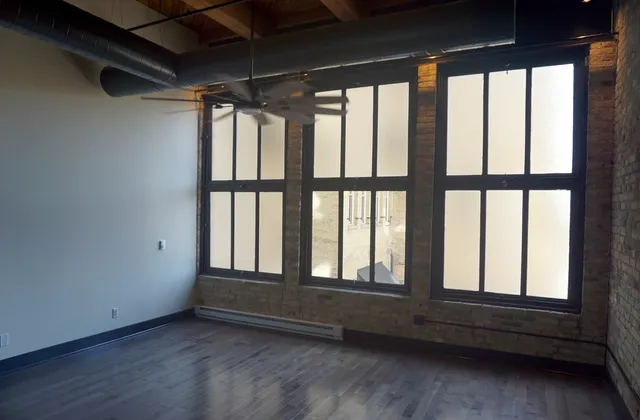 Large windows, brick wall and exposed ceiling structure in a Pritzlaff Building apartment room in Milwaukee, source-dated September 2025