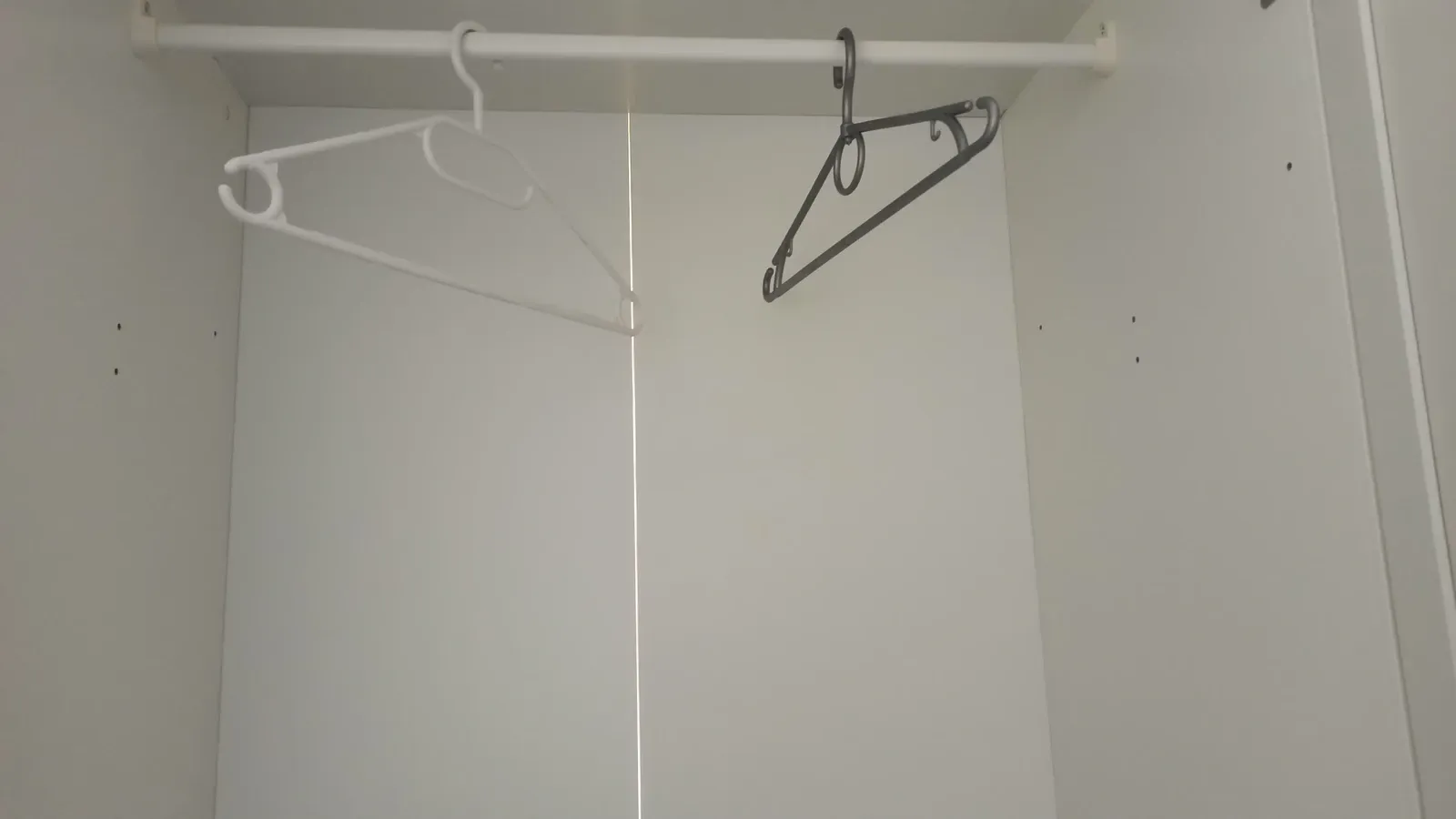 Two empty clothes hangers inside a wardrobe with a narrow light gap at the back, January 2023