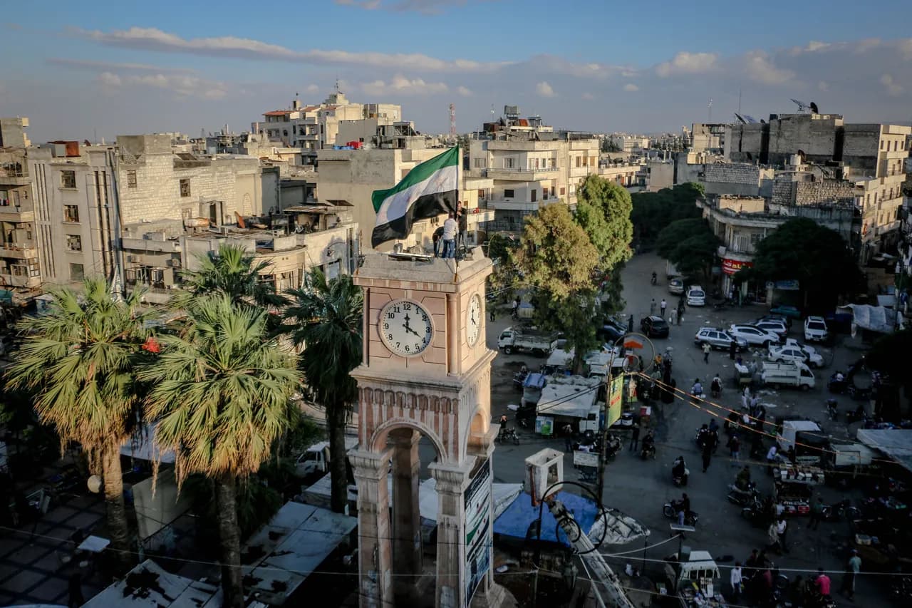 Elevated view of Idlib’s clock tower and surrounding city square, with palm trees, shops and residential buildings